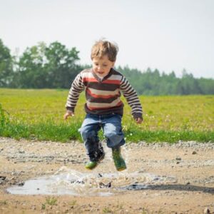 A cheerful child in a striped sweater jumps into a puddle on a sunny day in Czechia.